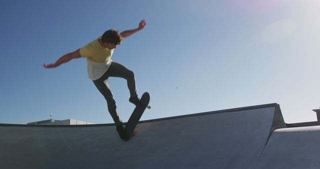 Young man performing a trick on a skateboard at a skatepark on a sunny day. Great for use in sports advertisements, youth-focused campaigns, or promoting an active lifestyle.