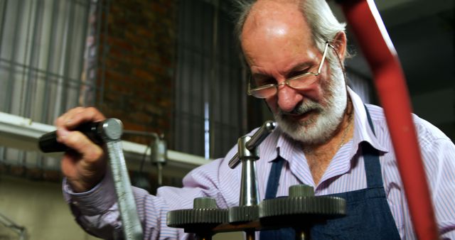 Image showcases senior craftsman operating precision machining tool in an industrial workshop environment. Best used for content related to manual labor, senior employment, skilled craftsmanship, engineering, workshops, and machinery. Ideal for educational materials, promotional content, or articles highlighting the importance of experienced professionals in manufacturing and mechanical industries.