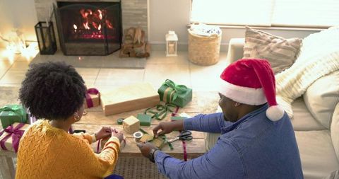 Couple Wrapping Holiday Presents by Fireplace, Santa Hat Cozy Living Room Gift Wrapping