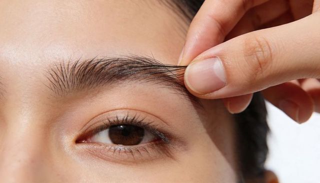 Plucking eyebrow hairs close-up revealing brown iris natural brow grooming beauty routine