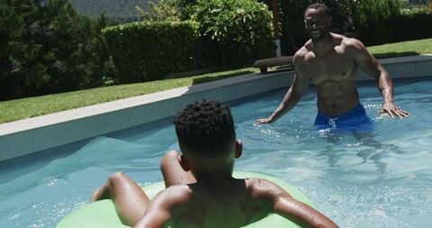 African american father and son playing on float in backyard pool summer fun and bonding