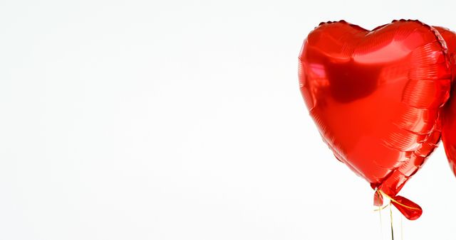 A shiny red heart-shaped balloon floats against a white background, with copy space. Its vibrant color and shape symbolize love and celebration, often associated with Valentine's Day or romantic occasions.