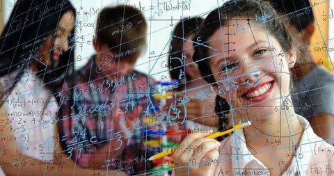 Smiling teen solving math on glass board collaborating with classmates learning stem