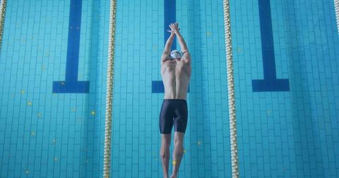 Competitive swimmer streamlining underwater between lane ropes in indoor pool