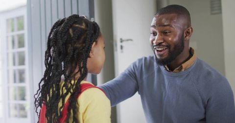 Smiling father greeting daughter at home door with red backpack, sharing warm moment