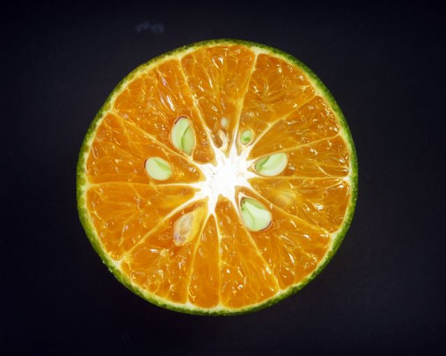 Close-up image showcasing the vibrant and fresh interior of an orange fruit against a black background. Ideal for use in health and nutrition-related content, advertisements for citrus products, or educational materials about fruits and vegetables.