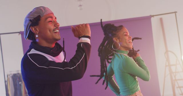 This image captures two young adults dancing joyfully in a studio with vibrant energy. They are stylishly dressed in casual urban streetwear, expressing joy and excitement. Ideal for use in campaigns promoting youth culture, joyfulness, nightlife, dance classes, or urban fashion brands.