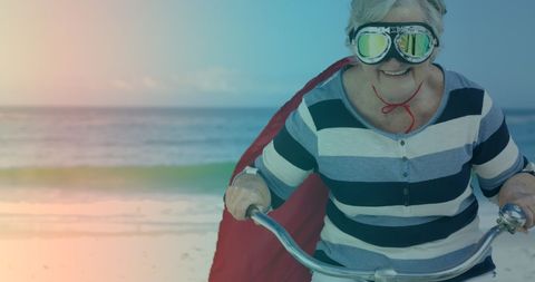Senior Woman Enjoying Bicycle Ride in Superhero Cape at Beach