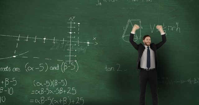 Image of a young Caucasian man celebrating in front of moving mathematical graphs and formulae written in chalk on a blackboard