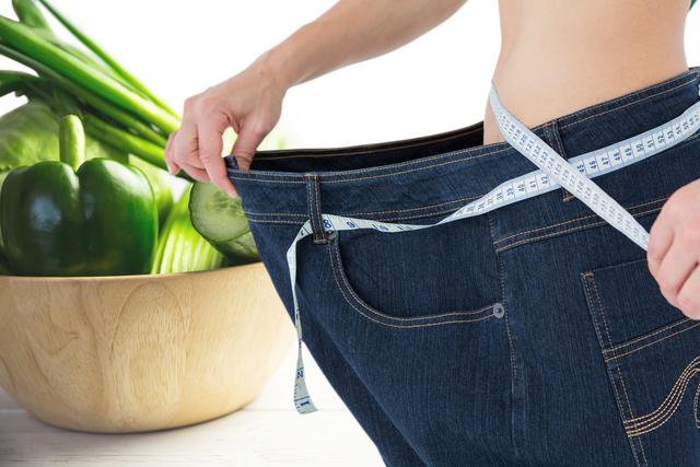 Digital composite of Midsection of woman wearing loose jeans with vegetables in background