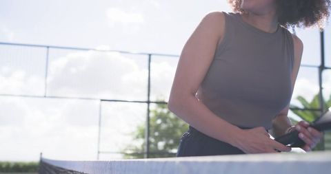Sunlit woman holding table tennis paddle beside outdoor ping pong table and net