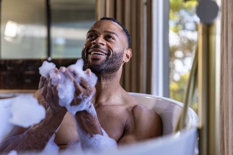 Mature man enjoying bubble bath in sunlit freestanding bathtub for self care and wellness