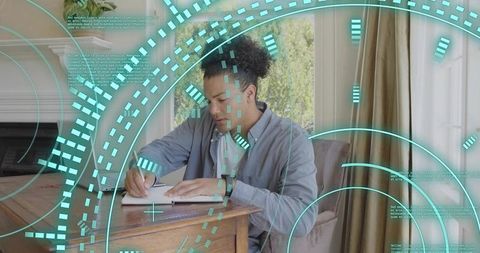 Young man writing in notebook at wooden desk with teal augmented reality hud overlay