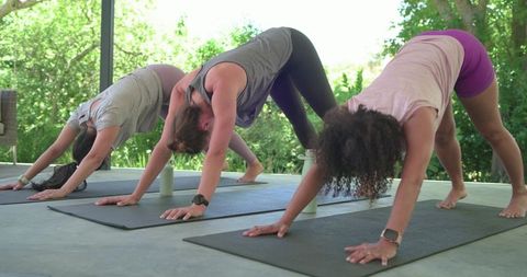 Multicultural women practicing outdoor yoga downward dog on patio for fitness and wellness