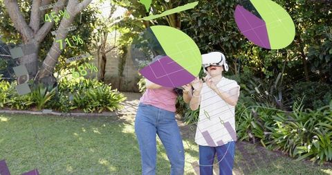 Middle-aged woman helping senior explore virtual reality with ar overlays in sunny backyard