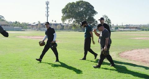 Men Walking on Sunlit Baseball Field Carrying Gloves and Helmet Showing Team Camaraderie