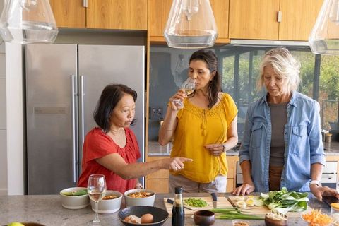 Multigenerational friends preparing dinner and tasting wine on sunlit kitchen island