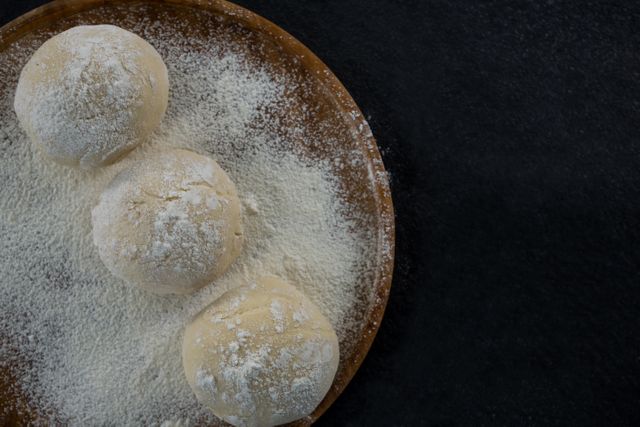 This image shows three pizza dough balls on a wooden rolling board dusted with flour. Ideal for use in food blogs, recipe websites, cooking tutorials, and culinary magazines. Perfect for illustrating homemade pizza preparation, baking techniques, and kitchen activities.