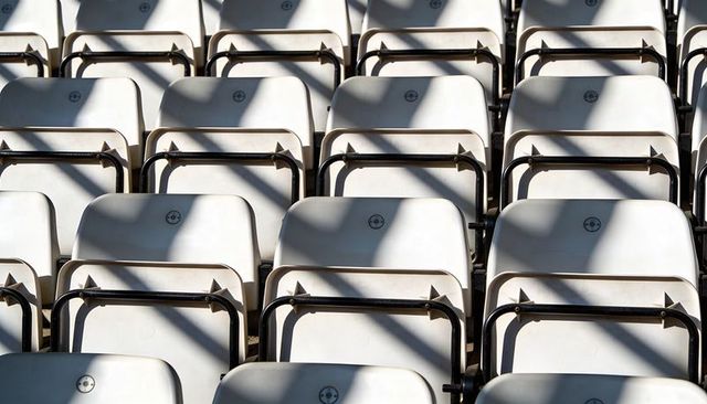 Empty white stadium seats casting diagonal shadows, repeating rows and geometric symmetry