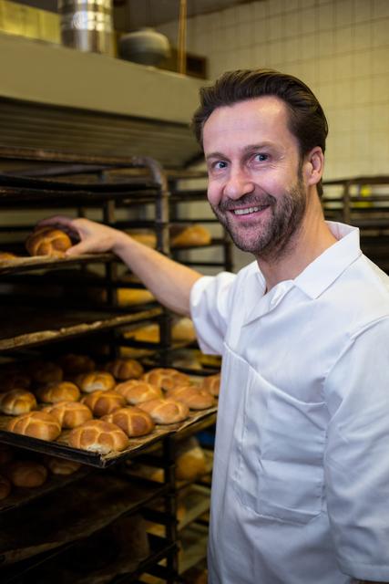 Smiling baker placing baked buns in shelf - Download Free Stock Photos Pikwizard.com