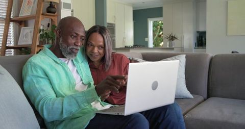 Mature black couple browsing laptop together on cozy sofa in modern open-plan living room