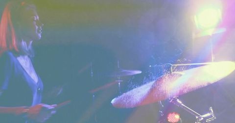 Female drummer hitting cymbal with spark spray under neon spotlight on live stage