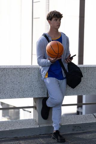 Teen athlete leaning on urban rooftop balancing basketball checking phone