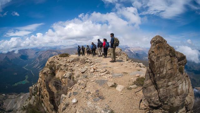 Group of hikers trekking narrow alpine ridge with panoramic mountain valley view