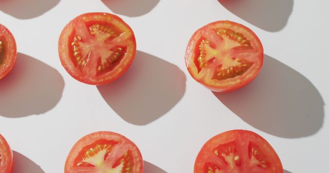 Freshly sliced tomatoes laying neatly on a white background, creating a vibrant pattern with their red color and texture prominently displayed. Perfect for use in food blogs, health and nutrition websites, cooking and recipe apps, or as background images in advertisements focused on fresh produce and healthy eating.