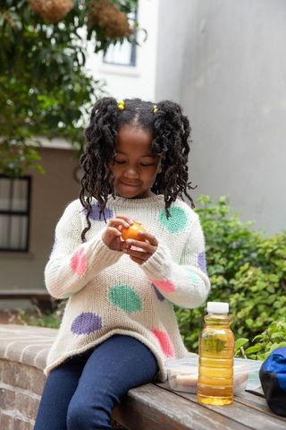 African american girl peeling orange in urban courtyard