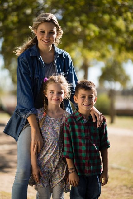 Mother and her two children enjoying a sunny day in the park. The family is smiling and dressed in casual clothing, surrounded by greenery. Ideal for use in family-oriented advertisements, parenting blogs, and lifestyle magazines.