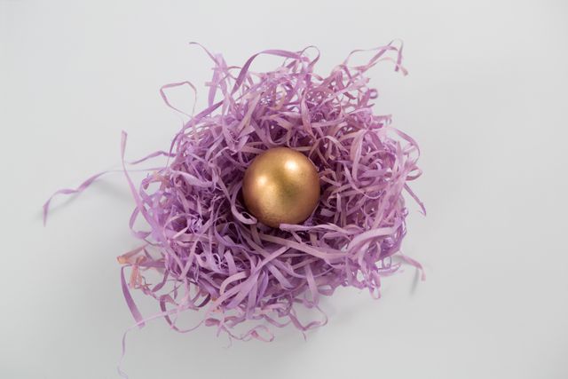 Golden Easter egg nestled in a purple paper nest on a white background. Perfect for Easter-themed promotions, holiday greeting cards, festive decorations, and spring celebration advertisements.