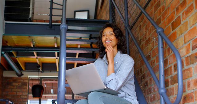 Smiling woman with laptop sitting on stair at home 4k