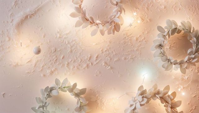 Cream-White Wreaths with Warm Fairy Lights on Textured Plaster Wall for Elegant Decor