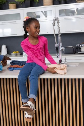 Young black girl sitting on kitchen island holding laundry smiling with parent hand