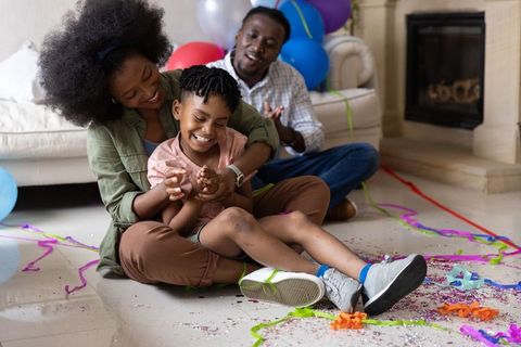African american family celebrating at home hugging smiling child with balloons and confetti