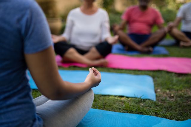 Group of people meditating on exercise mats in a park, focusing on relaxation and mindfulness. Ideal for promoting wellness, fitness, and healthy lifestyle activities. Suitable for use in articles, advertisements, and social media posts related to yoga, meditation, and outdoor fitness.