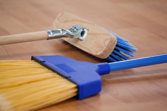 Close-up of two brooms lying on a wooden floor, perfect for illustrating household cleaning, domestic chores, and home maintenance. Ideal for use in articles, blogs, or advertisements related to cleaning products, home care tips, and DIY home improvement.