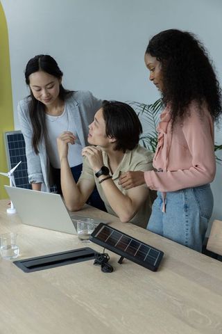 Diverse team collaborating on solar and wind energy prototype with laptop in minimal office