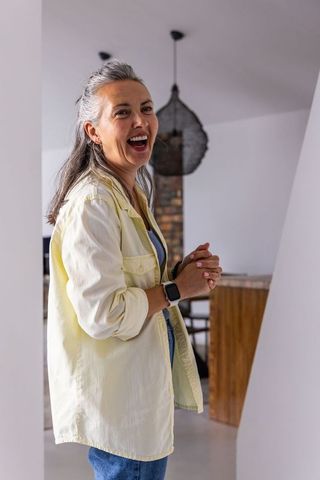 Mature woman laughing in modern open-plan kitchen wearing smartwatch and casual outfit