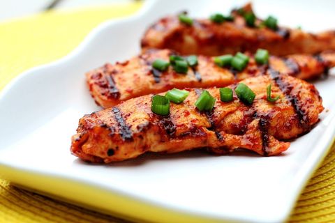 Grilling spicy glazed chicken tenders garnishing with chopped green onions on white plate