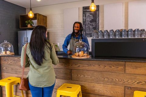 Barista serving customer at modern coffee counter with pastries under glass cloches