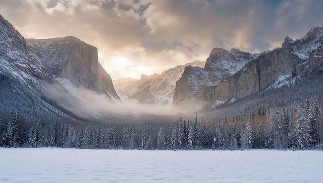 Sunrise illuminating snowy alpine valley with misty granite cliffs and frosted pine forest