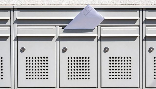 Sunlit mailbox row with white envelope protruding from slot casting sharp shadow