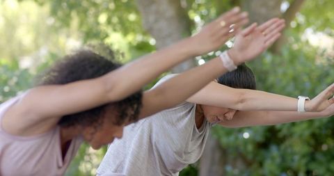 Diverse women practicing standing forward stretch in sunlit park for wellness and fitness