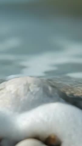 Approaching wave enveloping ridged seashell on pebbles closeup vertical ocean shore