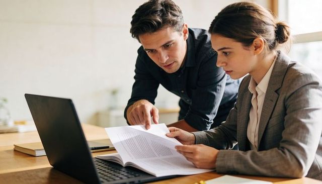 Business professionals reviewing contract and collaborating at laptop in modern office