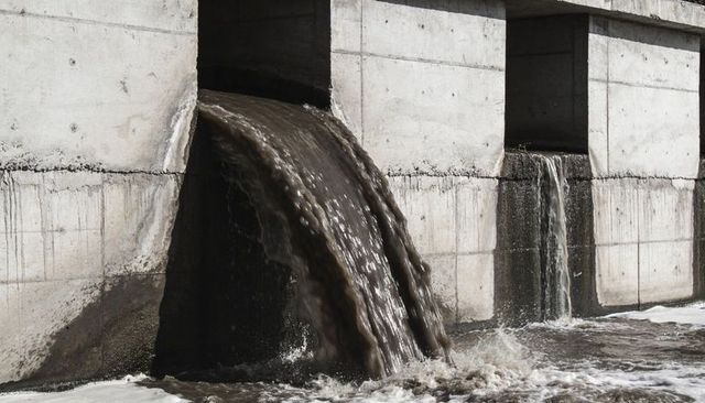 Muddy water pouring from concrete spillway into turbulent channel with foam