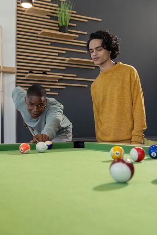 Diverse young men playing pool in modern lounge taking shot on green table