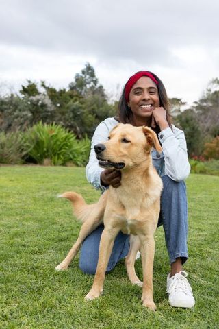 Asian woman kneeling in park holding golden dog, smiling, casual outdoor companionship